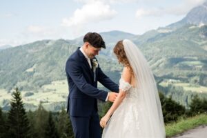Groom holding the bride’s dress while both look down at it smiling