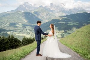 Groom holding his bride’s arm while they smile at each other
