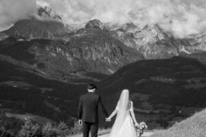 Black-and-white photo of a wedding couple walking hand in hand toward the mountains