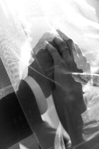 High-contrast close-up of a wedding couple’s hands beneath the veil with focus on the ring