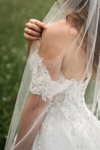 Close-up over the bride’s shoulder while she holds her veil
