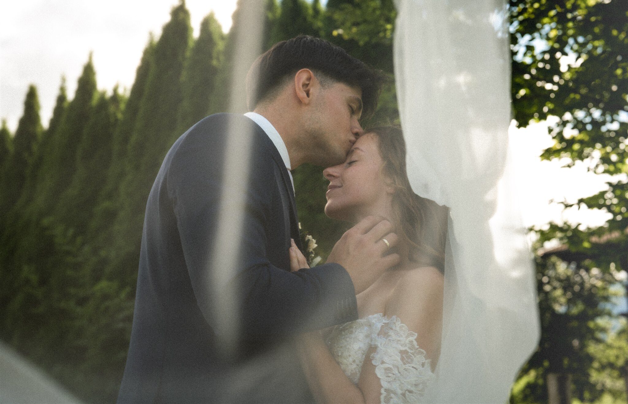 Vintage photo of a wedding couple beneath the veil while the groom kisses the bride on the forehead