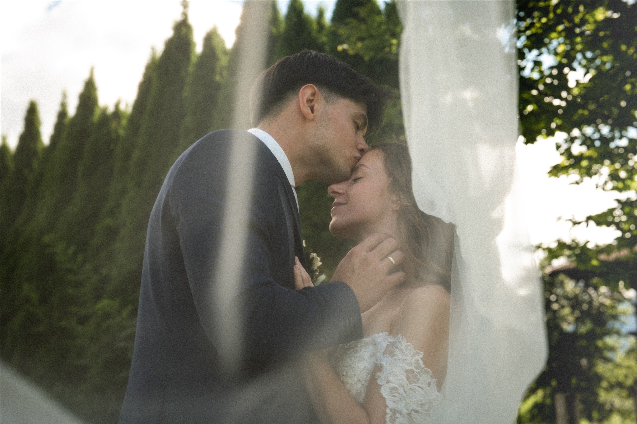Vintage photo of a wedding couple beneath the veil while the groom kisses the bride on the forehead