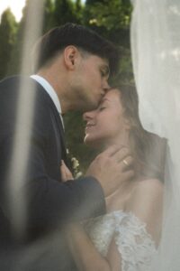 Portrait-format vintage grainy photo of a groom kissing his bride on the forehead