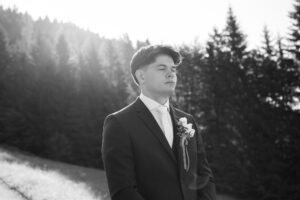 Vintage black-and-white photo of a nervous groom with closed eyes standing before trees in sunlight