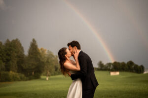 Passionate kiss of the bride and groom in front of a rainbow