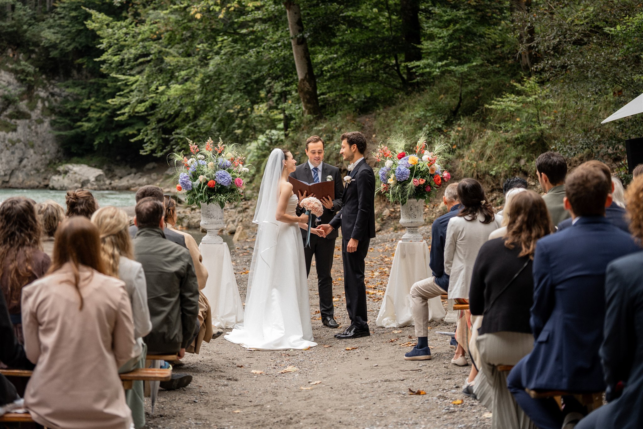 Wedding couple during an outdoor ceremony on a riverbed, photographed from the ceremony aisle