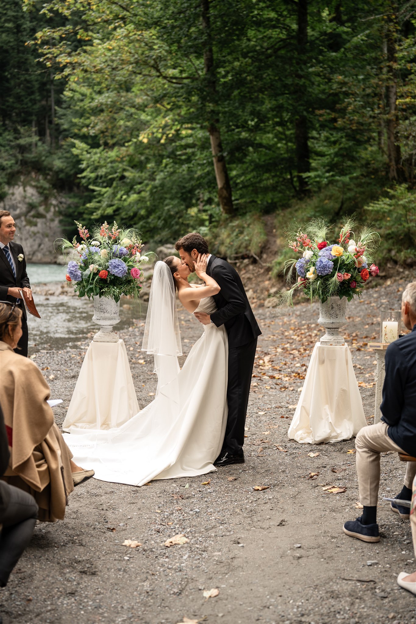 Wedding kiss on a riverbed framed by two floral arrangements