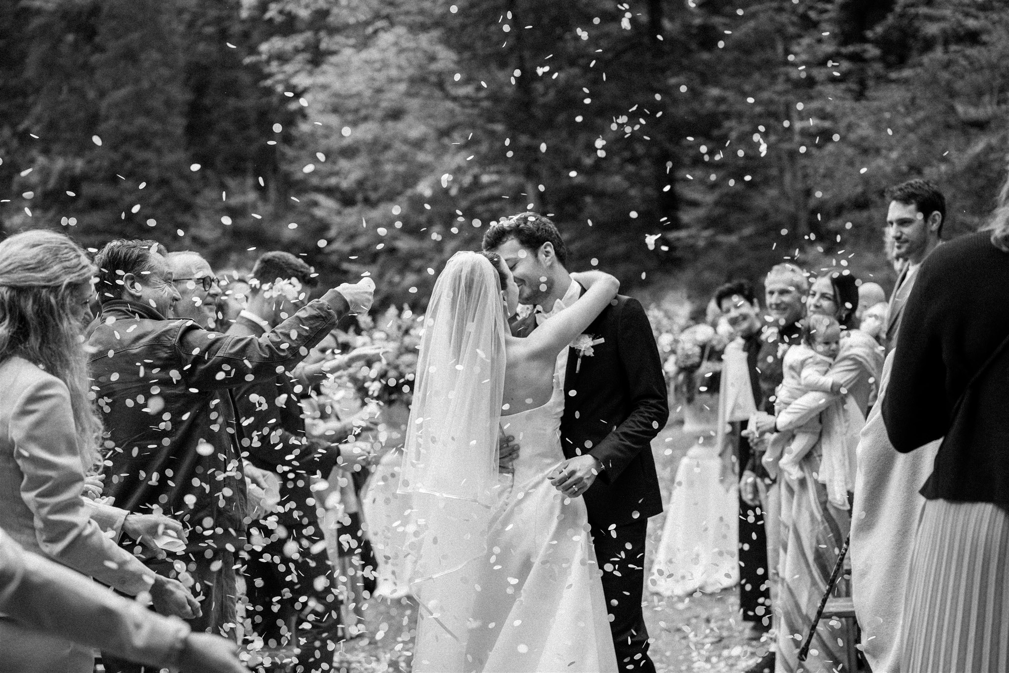 Wedding couple kissing during their exit surrounded by cheering guests and confetti