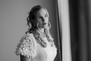 Black and white photo of the bride gazing dreamily out the window