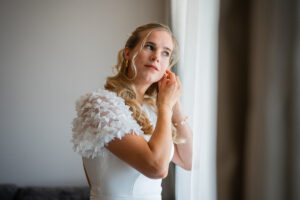 The bride standing by the window adjusting her earrings