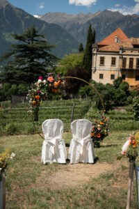 Close-up of the ceremony setup at Schloss Rametz with wedding arch, vineyards, mountains, and castle in the background