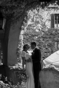 Black and white photo of a bride and groom kissing beneath an archway in the courtyard of Castle Rametz