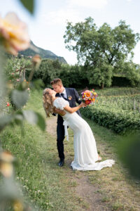 Groom dipping his bride backward on a path between vineyards while sharing a romantic kiss