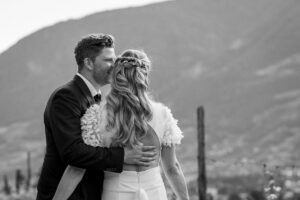 Black and white photo of a groom hugging his bride and kissing her on the cheek