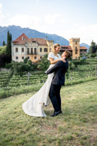 Wide-angle photo of a groom lifting and spinning his bride in front of Castle Rametz