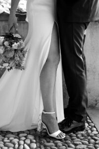 Black and white close-up of a bride and groom's legs, with the bride extending her leg through the slit of her dress
