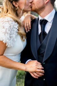 Close-up of a bride and groom sharing a romantic kiss while holding hands