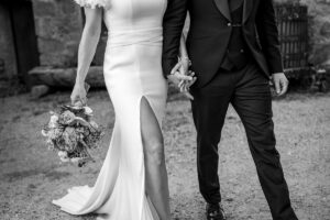 Black and white photo of the lower bodies of a bride and groom walking hand in hand along a path