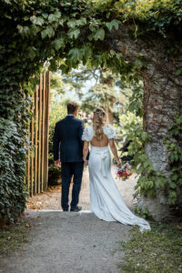 Bride and groom walking through a hedge arch toward their wedding guests
