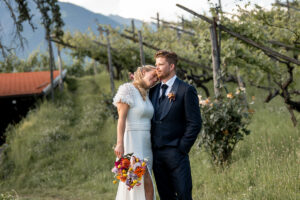 Bride resting her head on her husband's shoulder in front of the vineyard rows in South Tyrol