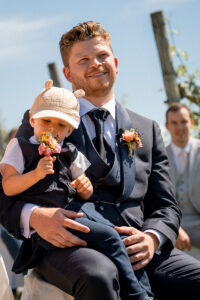 The groom looks ahead during the ceremony while his son plays on his lap