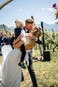 Wedding kiss in front of the vineyards with the couple's child held between them