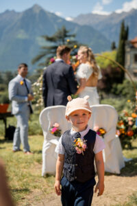 A child stands in the aisle while the wedding couple stands arm in arm looking toward the mountains