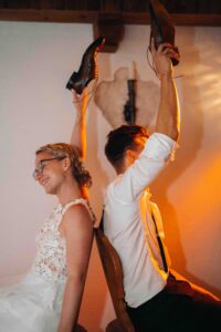 Wedding couple playing the “Who is more likely to?” shoe game, both laughing while holding up the groom’s shoe