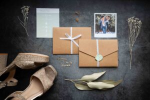 Flatlay of wedding details with invitation, shoes, jewelry, and a photo of the couple