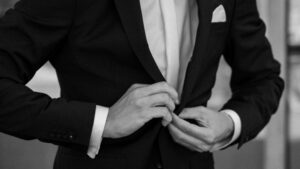 Black-and-white detail photo of the groom buttoning his suit