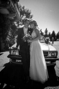 Vintage black-and-white photo of the wedding couple leaning against a vintage car