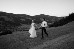 Black-and-white wide-angle photo of the wedding couple walking with mountain views