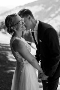 Black-and-white photo of a groom whispering into his bride’s ear