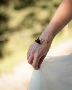 Detail photo of the bride’s hand holding her dress with a butterfly resting on it