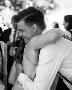 Side-view black-and-white photo of an embrace between the groom and a friend