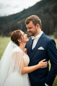 Wedding couple in a field with mountains in the background, looking lovingly into each other’s eyes