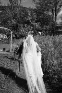 Black-and-white photo of a bride from behind with a long veil and dramatic lighting