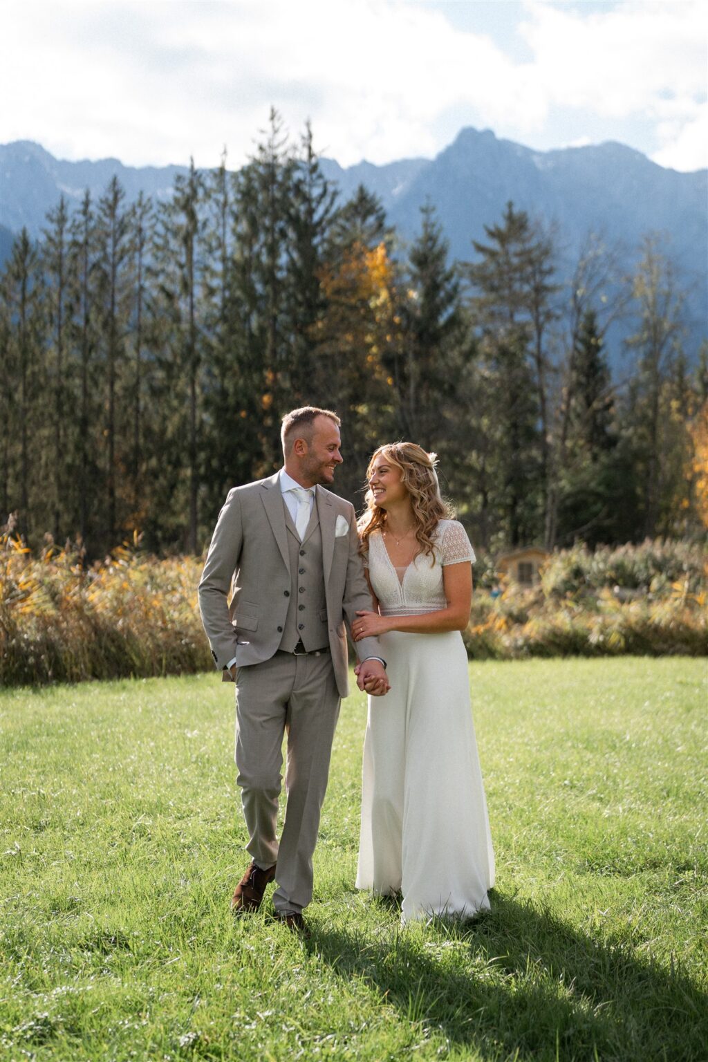 Wedding couple in Walchsee happily walking arm in arm across a field with the Wilder Kaiser in the background