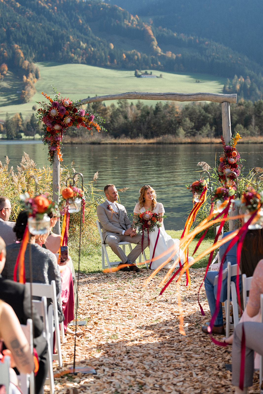 View from the ceremony aisle of the wedding couple beneath the arch at Lake Walchsee