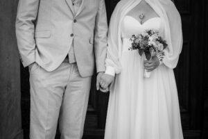 Black-and-white close-up of a wedding couple’s upper bodies while holding hands