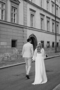 Black-and-white photo of a wedding couple from behind walking through the old town