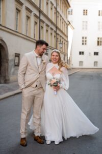 Wedding couple standing in the old town while the groom looks at the bride and she smiles at the camera