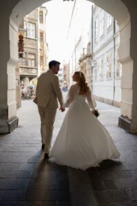 Wedding couple walking hand in hand through an archway in Innsbruck’s old town while looking at each other