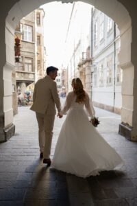 Wedding couple walking hand in hand through an archway in Innsbruck’s old town while looking ahead