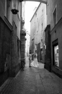 Black-and-white photo of a wedding couple in the old town while the groom twirls the bride