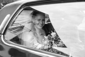Black-and-white photo of the bride smiling through the Cadillac window with reflections in the glass
