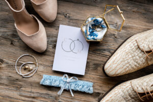 Flat lay of invitation, shoes, garter, jewelry, and wedding rings arranged on a stylish surface