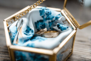 Close-up of wedding rings inside a glass container with decorative floral fabric