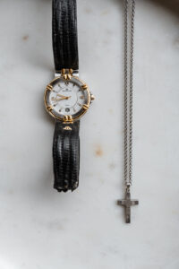 Flat lay of a wristwatch and cross necklace displayed on an elegant marble surface